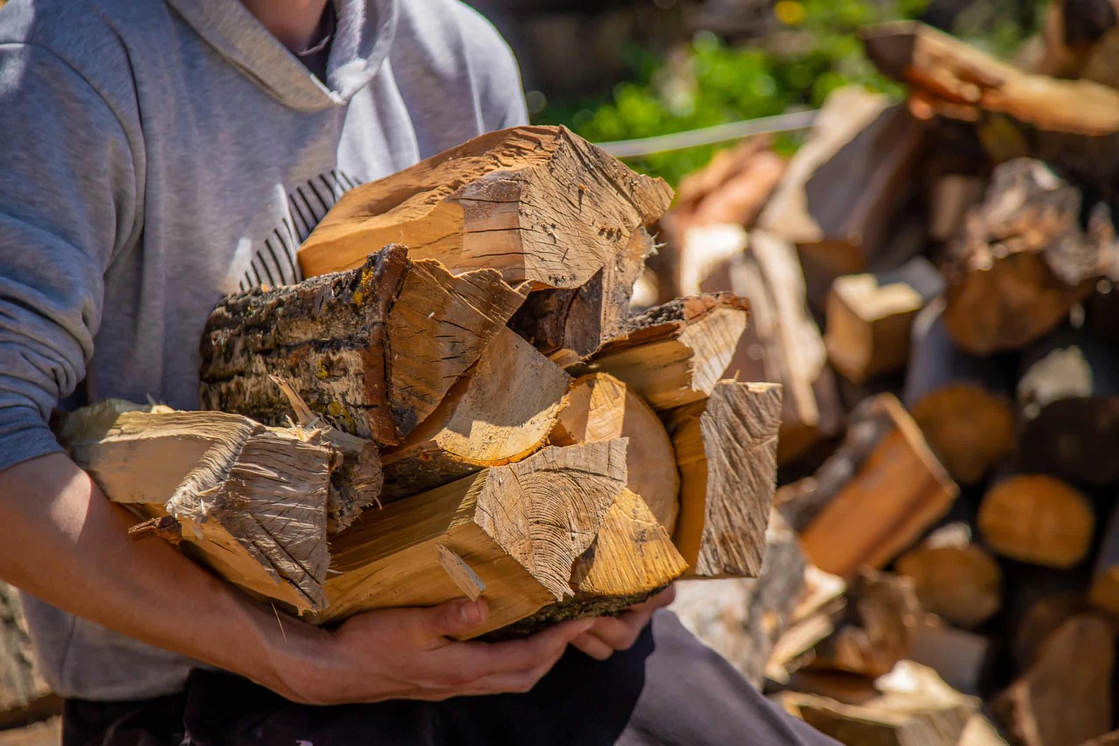a pile of stacked firewood, prepared for heating the house. gathering fire wood for winter or bonfire. man holds fire wood in hand. selective focus