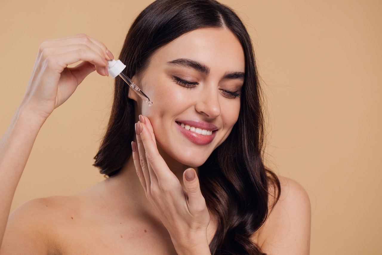 woman,dropping,serum,on,face,on,beige,background.,european,girl